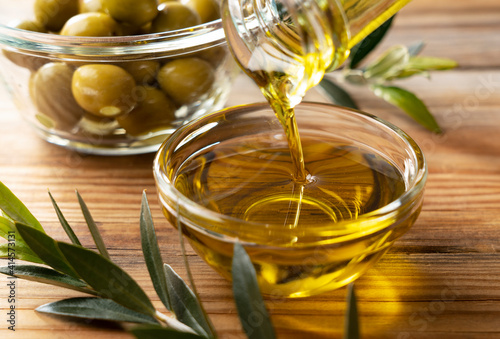 Pour olive oil into a glass bowl set against a wooden background