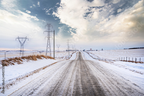 A rural gravel road along power lines and electrical transmission towers in Rocky View County Alberta Canada during the winter