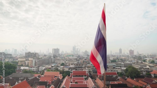 4k Thailand state flag fluttering in the wind on the top of Wat Saket Golden Mountain with Bangkok at the Background. Slow motion View over Bangkok with waving Thai flag. Rooftop of Wat Saket photo