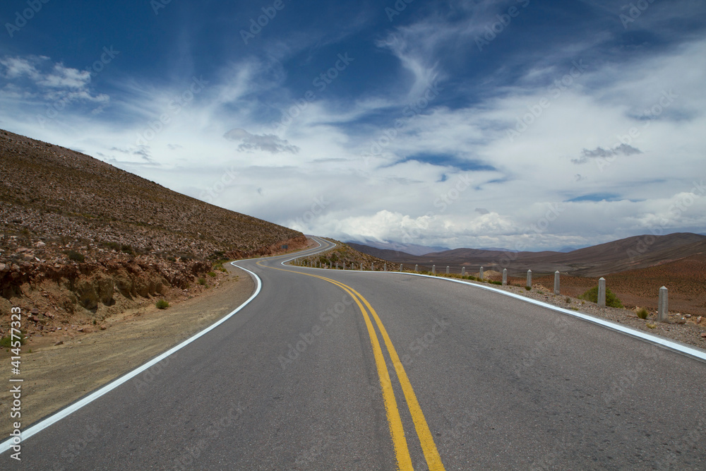 Road trip into the wild. View of the asphalt highway across the desert and mountains under a beautiful sky. 