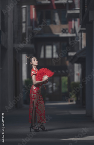 Beautiful Asian woman, model,  wearing traditional red cheongsam qipao dress holding red foldable feather fan in China Town for Chinese new year concept. photo