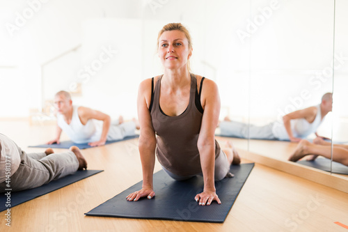Positive woman exercising yoga with group of young sporty people in studio