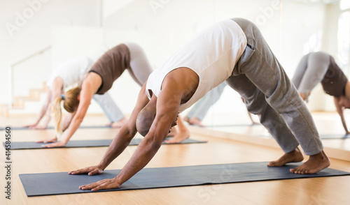 Portrait of focused man making yoga exercises with friends at fitness center photo