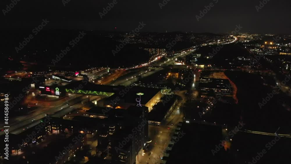Stunning night-time aerial descending above downtown Partille and European route E6 highway with illuminated skyline, buildings and street lights in Gothenburg City, Sweden. Stunning night-time aerial descending above downtown Partille and European route E6 highway with illuminated skyline, buildings and street lights in Gothenburg City, Sweden.
