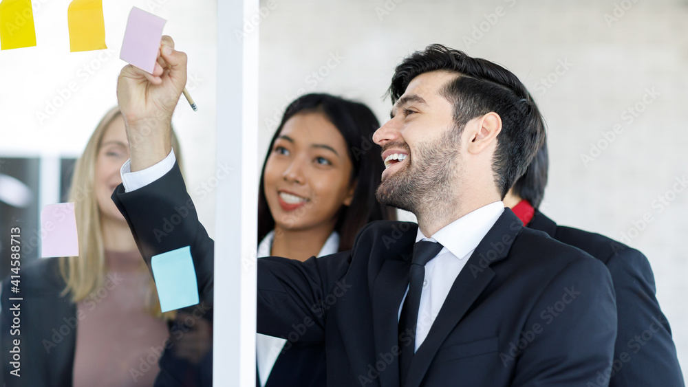 Selective focus on Caucasian Businessmen and Asian Businesswomen smiling explaining working smilling and on a board, having post-it papers at the conference room in the office. Selective focus on Caucasian Businessmen and Asian Businesswomen smiling explaining working smilling and on a board, having post-it papers at the conference room in the office.