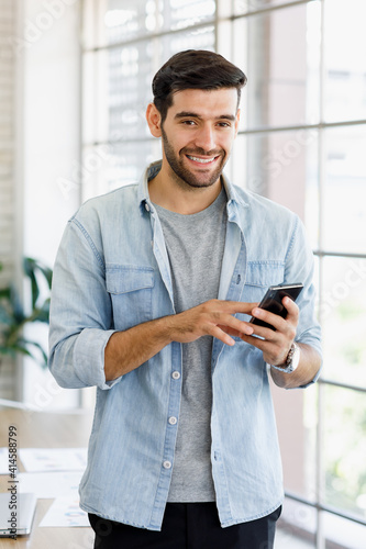 Image is portrait. Smiling handsome Caucasian businessmen standing and using smartphone is working in the room at the office. Concept Smile working cozy.