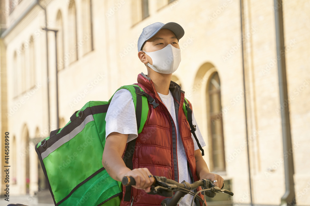 Young asian male courier with thermo bag wearing face protective Young asian male courier with thermo bag wearing face protective