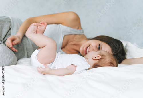 Young mother having fun with cute baby girl on bed with white linen, natural tones, love emotion