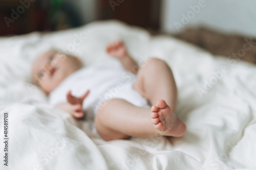 Cute baby girl 2-4 month on bed with white linen, natural tones, selective focus