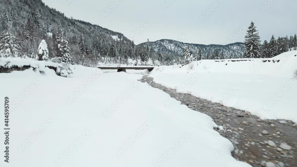 Aerial flying over frozen river on mountain valley and passing beside man standing on a bridge Aerial flying over frozen river on mountain valley and passing beside man standing on a bridge