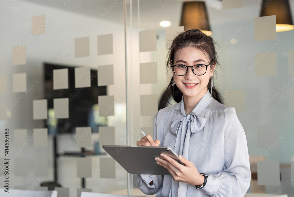 Asian young woman. Looking at camera holding a tablet at the office.