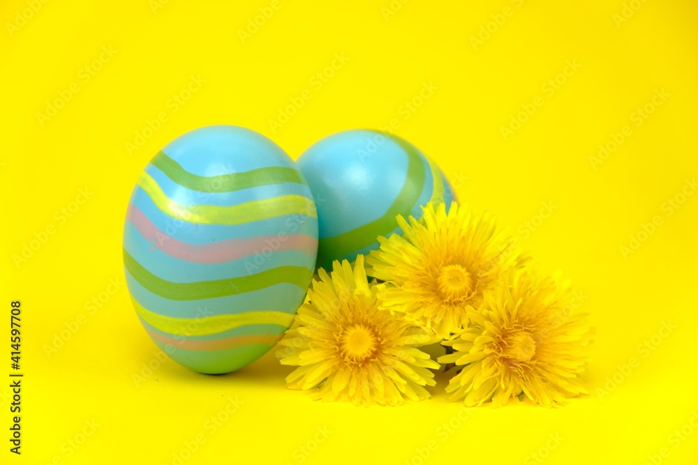 Easter holiday.Blue striped eggs,  dandelion flowers on a bright yellow background.Spring religious holiday background. copy space. 
