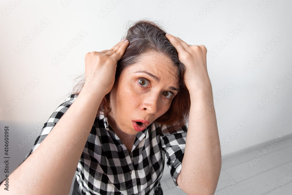 Horrified young woman looking in mirror staring open mouthed at the first grey hair, a first sign of ageing. Horrified young woman looking in mirror staring open mouthed at the first grey hair, a first sign of ageing.