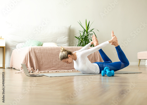 Online stretching home class. Adult caucasian woman lie on the mat in bow pose in front of the laptop, selective focus.