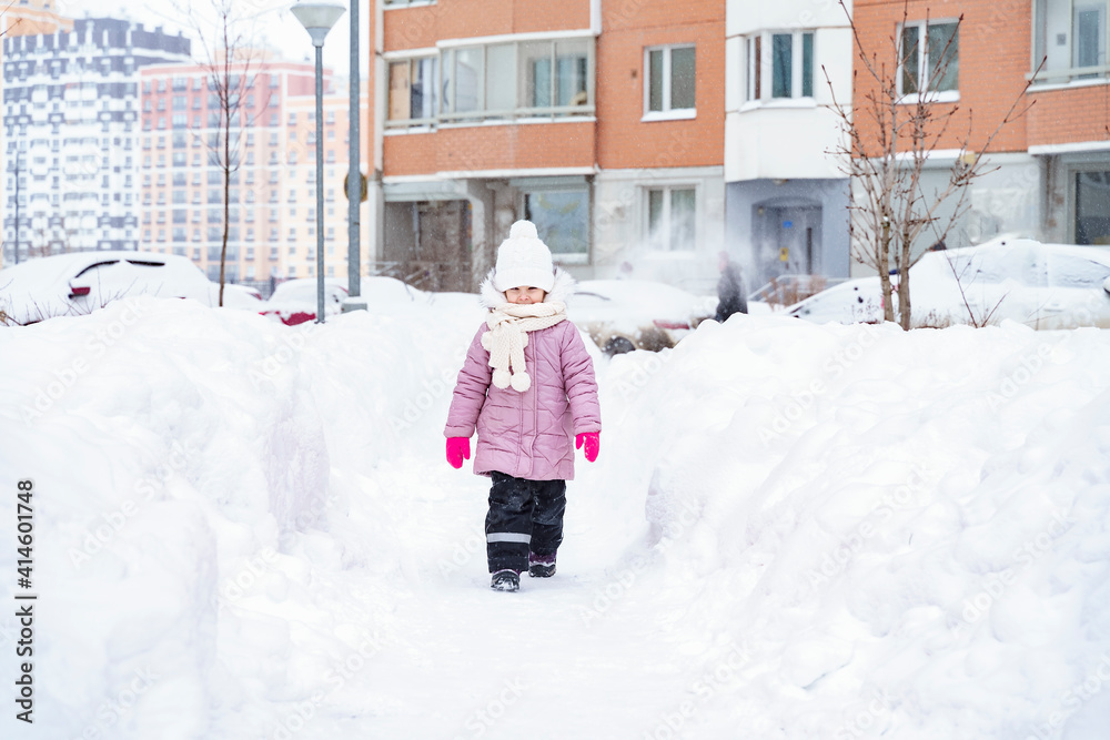 a little girl in a pink coat walks through the yard covered with snowdrifts