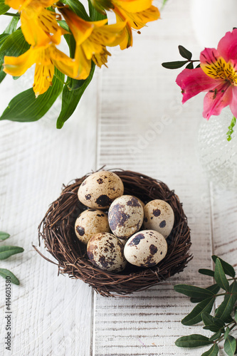 Quail eggs in a nest on a background of flowers. The concept of Easter, spring greeting card.