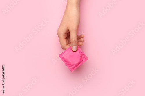 Female hand with wrapped condom on color background