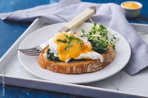 Slika na platnu Plate with tasty sandwich and florentine egg on color  background, closeup
