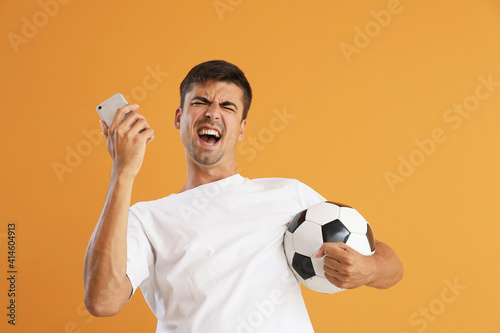 Fotobehang Happy man with cellphone and ball after winning of his sports bet on color backg