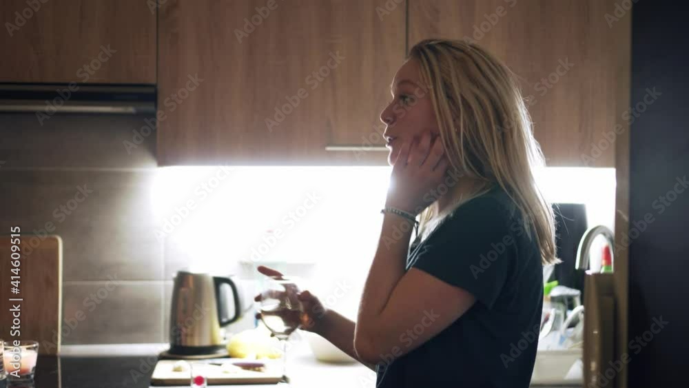 Girl drinking glass of white wine and singing in kitchen, house party Girl drinking glass of white wine and singing in kitchen, house party