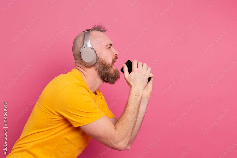 Handsome man in casual singing with mobile phone headphones isolated on pink background Handsome man in casual singing with mobile phone headphones isolated on pink background
