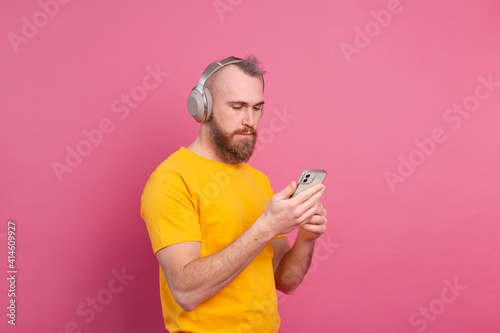 Handsome man in casual listening to music with headphones isolated on pink background © Анастасия Каргаполов