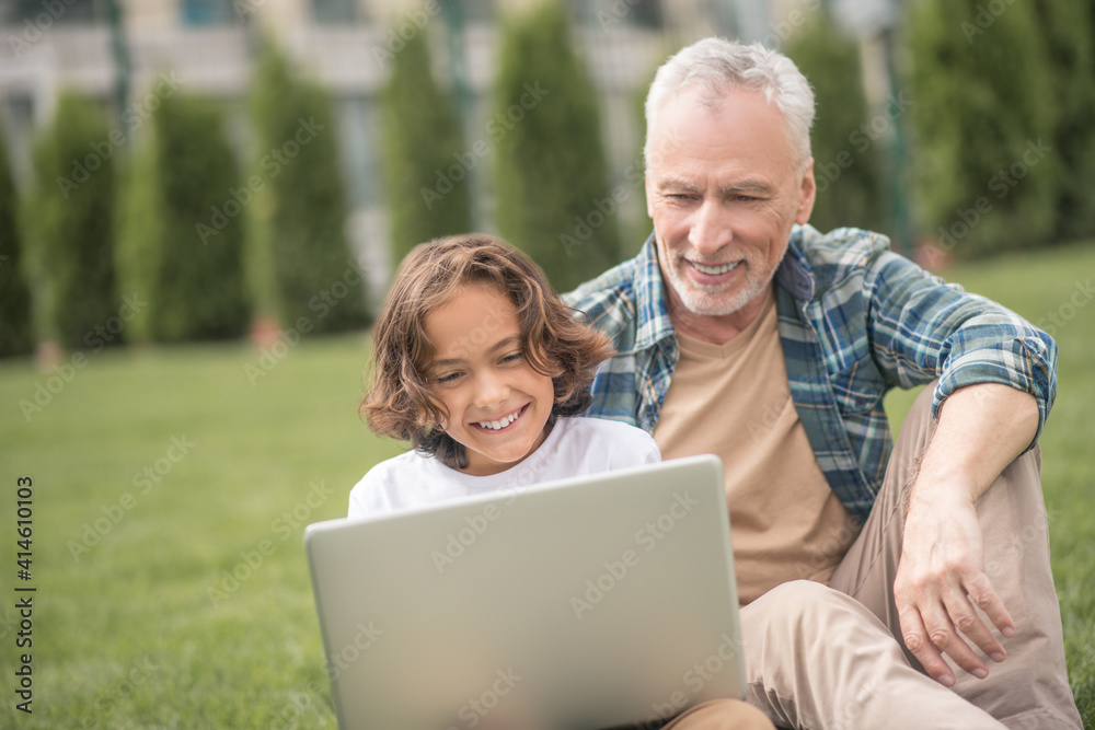 Son and dad sitting together with a laptop and having a video call Son and dad sitting together with a laptop and having a video call
