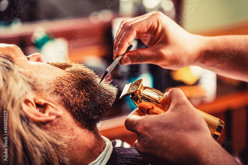 Barber works with a beard clipper. Hipster client getting haircut. Hands of a hairdresser with a beard clipper, closeup