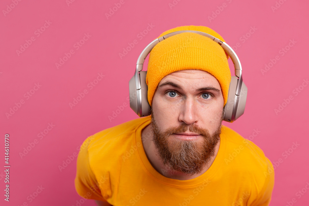 Fototapeta premium Handsome man in casual listening to music with headphones isolated on pink background