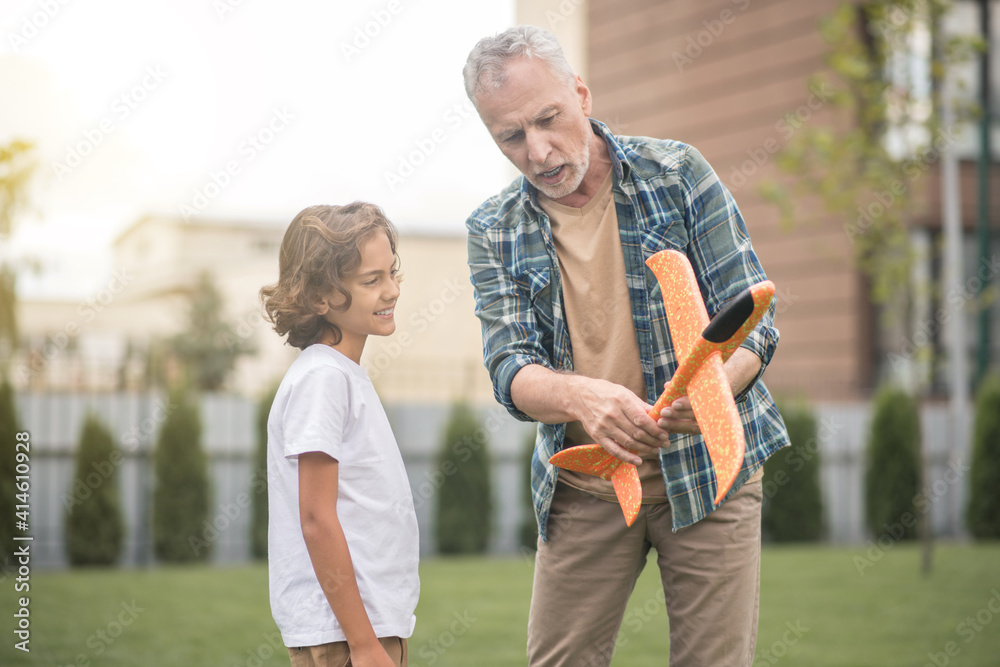 Gray-haired dad showing to his son how to use the toy plane