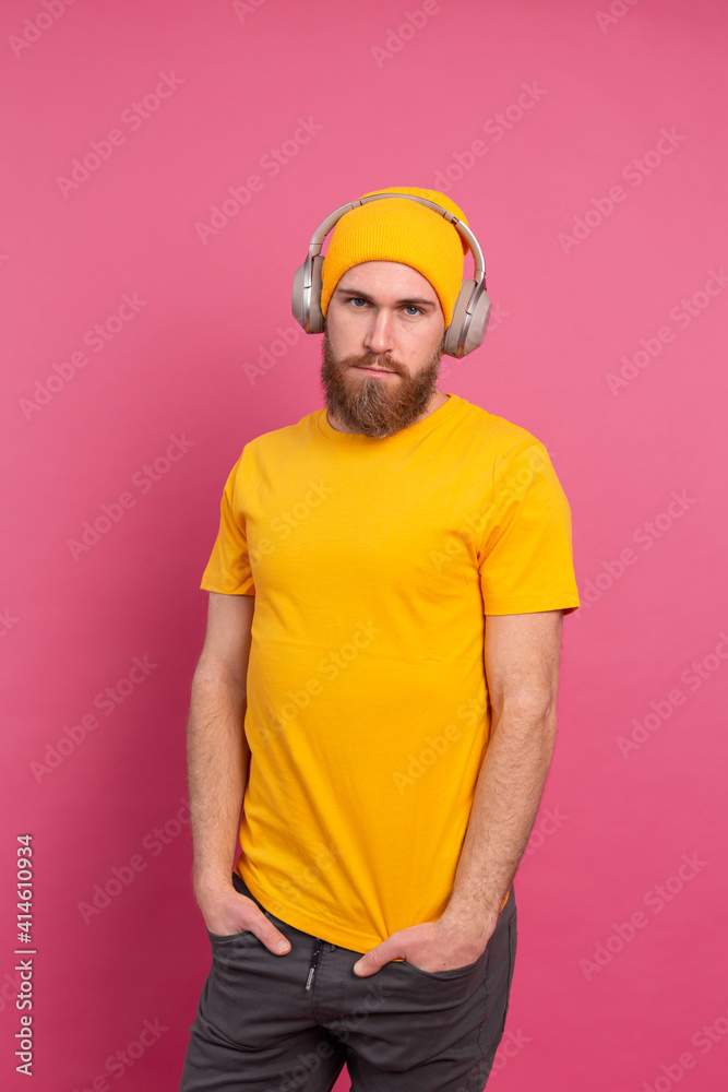 Handsome man in casual listening to music with headphones isolated on pink background