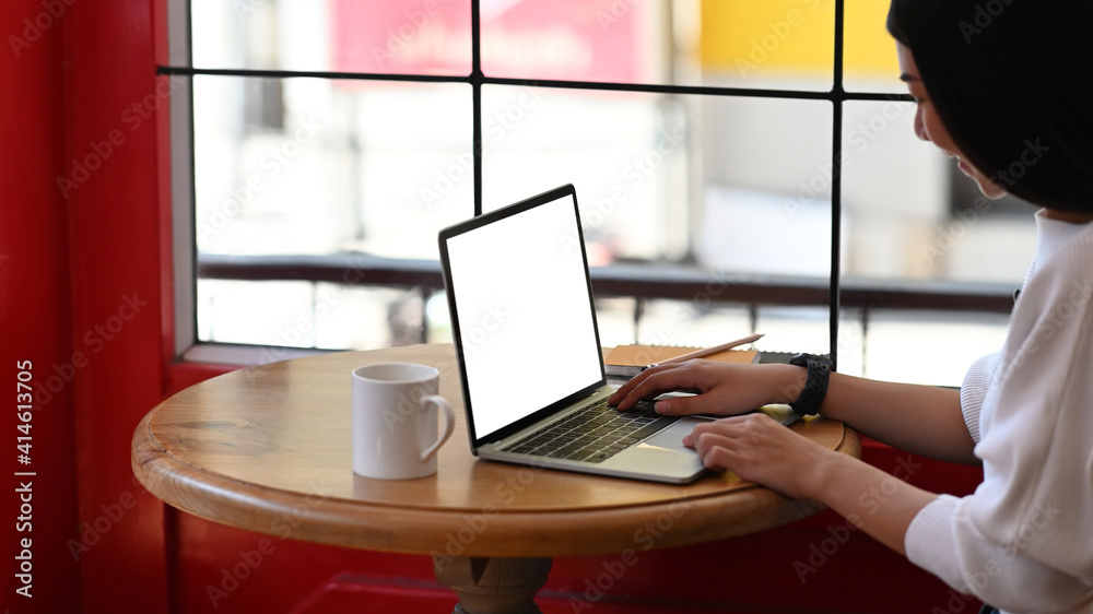 Fototapeta premium Cropped shot of smiling young woman entrepreneur working on her project with computer laptop at coffee shop.