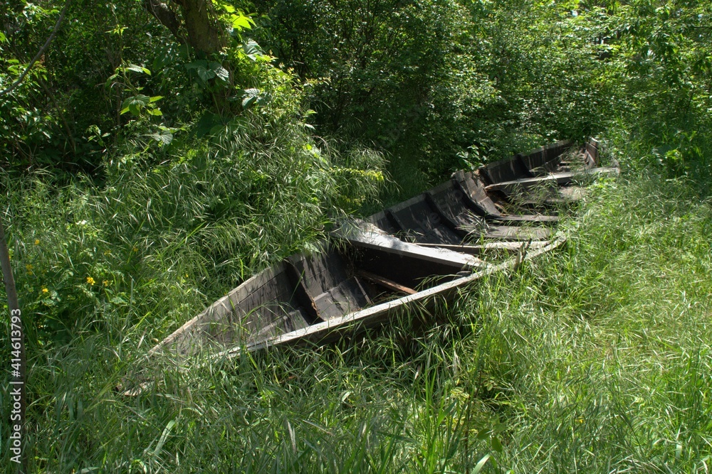 An abandoned old wooden boat lying in the grass near the river . An abandoned old wooden boat lying in the grass near the river .