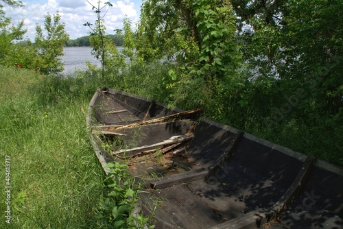 An abandoned old wooden boat lying in the grass near the river .