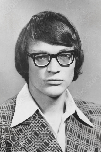 Portrait of young Soviet guy with glasses, in checkered jacket. Vintage black and white paper photo, 1970s. Transferred property, family archive. Outdated quality
