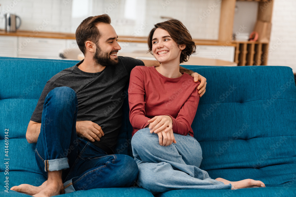 Happy young couple hugging and using remote control while watching TV Happy young couple hugging and using remote control while watching TV