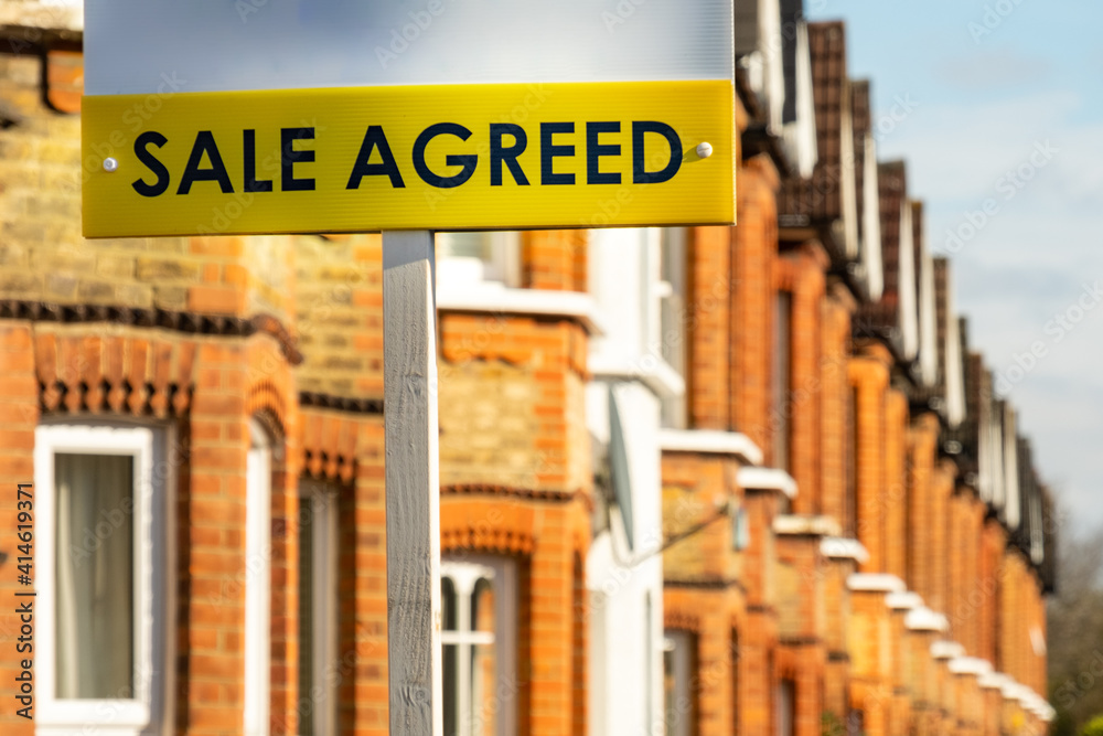 Naklejka premium Estate agent 'Sale Agreed' sign on street of red brick houses 