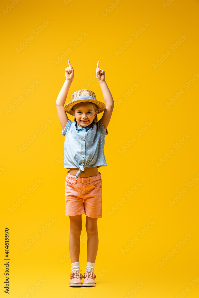 full length of cheerful child in straw hat pointing up with fingers on yellow full length of cheerful child in straw hat pointing up with fingers on yellow