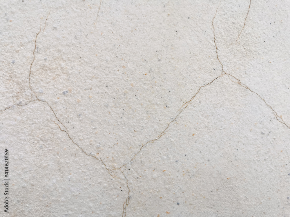 Fototapeta premium stone wall texture. Beige cracked cement with fine gravel surface. Ferruginous cracks on plaster wall. Old stucco wall with marble grains and rusty cracks.