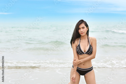 Portrait of young asian beautiful and sexy woman in black bikini sitting on the beach and looking camera. Cute girl having fun on holiday vacation with happy smiling face. Free space for advertising.