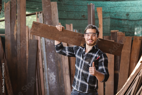 Fotografie Young carpenter caucasian man worker holding wood carry on the back, portrait man worker eye contact camera