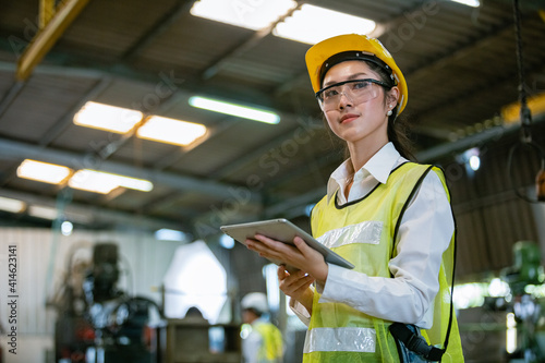 Fotografie portrait asian woman engineer industry heavy worker wearing hardhat and holding tablet standing at machine area in factory, engineering industrial concept