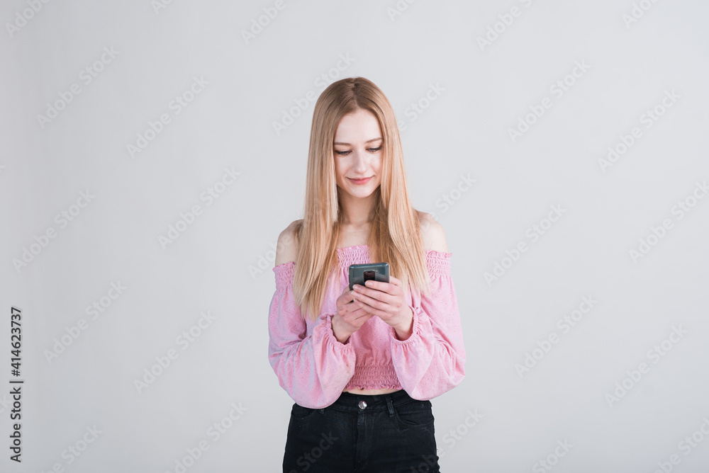 Portrait of a blonde girl holding a smartphone and texting in the studio on a white background Portrait of a blonde girl holding a smartphone and texting in the studio on a white background