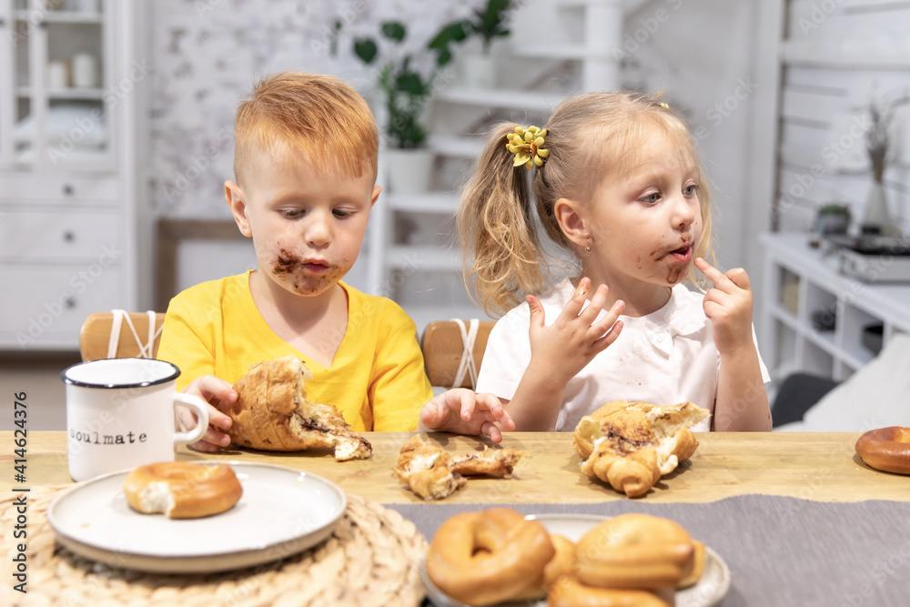 little red boy and a little girl eat croissants. the kids got dirty in chocolate. brother and sister have breakfast little red boy and a little girl eat croissants. the kids got dirty in chocolate. brother and sister have breakfast
