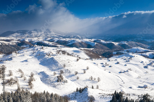 Fototapeta Naklejka Na Ścianę i Meble -  Aerial scenic rural view of Sirnea village at the bottom of Piatra-Craiului Mountains in freezing winter landscape from Romania
