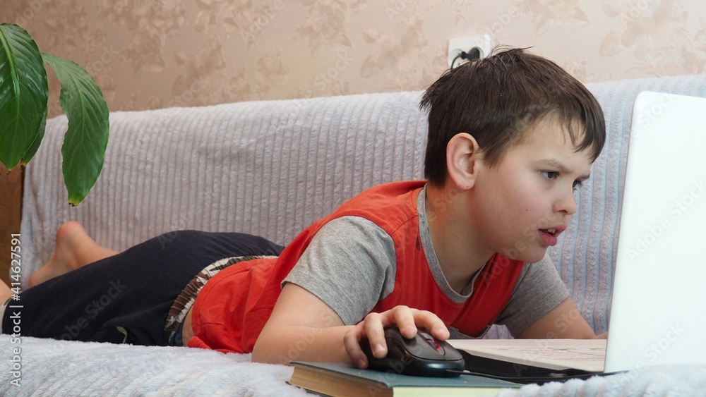 boy using a laptop for playing online games and wearing headphone at home, a boy at a computer or tablet at home on the couch, communicating with friends, blogging, studying online boy using a laptop for playing online games and wearing headphone at home, a boy at a computer or tablet at home on the couch, communicating with friends, blogging, studying online