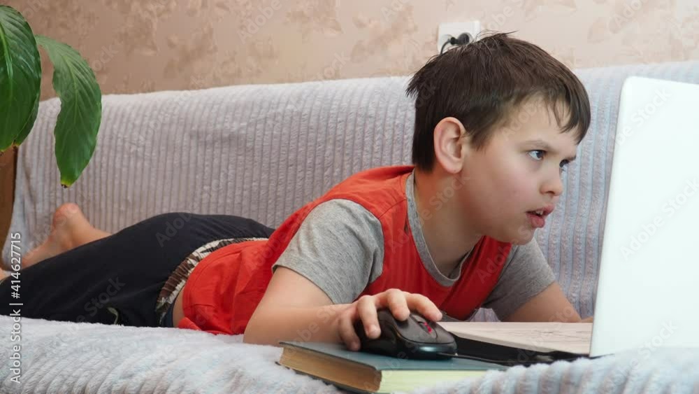 boy using a laptop for playing online games and wearing headphone at home, a boy at a computer or tablet at home on the couch, communicating with friends, blogging, studying online boy using a laptop for playing online games and wearing headphone at home, a boy at a computer or tablet at home on the couch, communicating with friends, blogging, studying online
