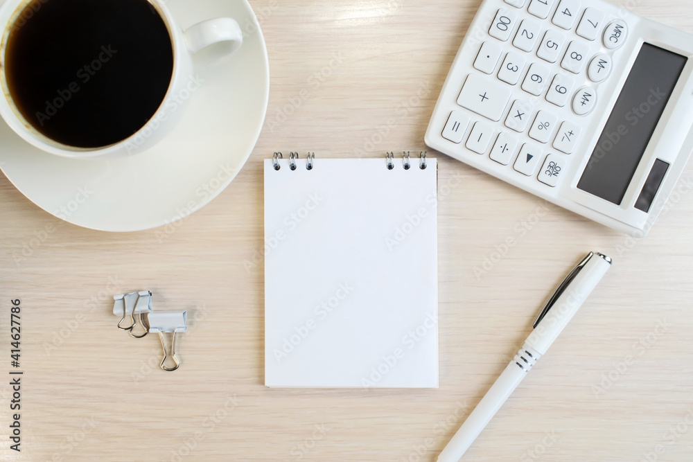 An office desk with a notebook that sits next to a coffee cup and a pen with a calculator on a wooden table. Space for the text. Business concept An office desk with a notebook that sits next to a coffee cup and a pen with a calculator on a wooden table. Space for the text. Business concept