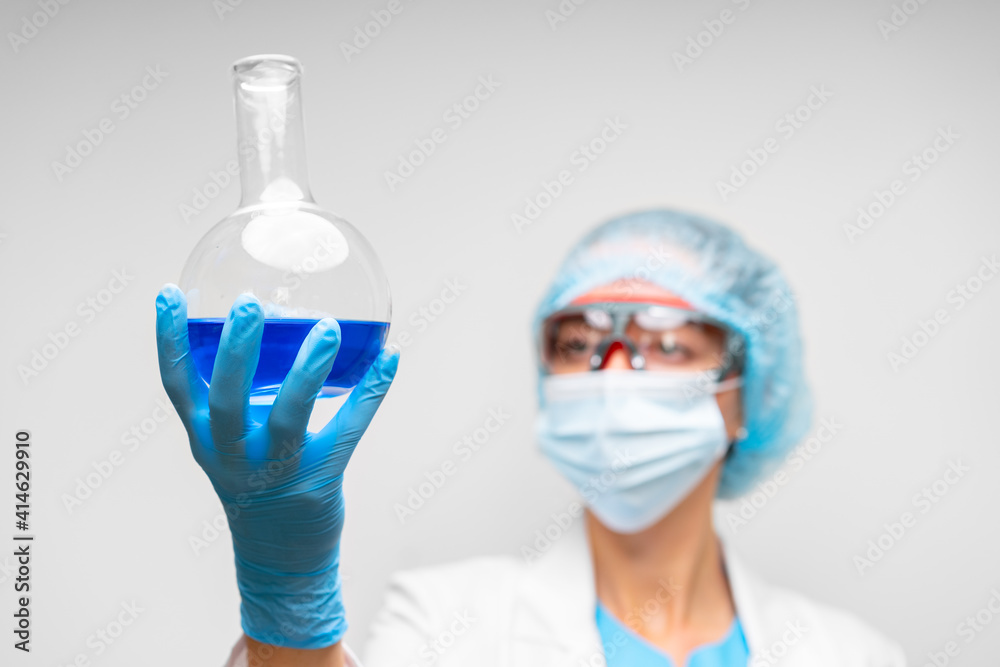 Woman scientist holding laboratory flask with chemical liquid, gray background Woman scientist holding laboratory flask with chemical liquid, gray background