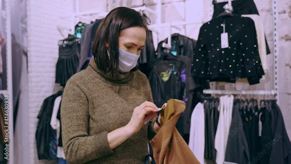 Shopping during quarantine. An attractive woman wearing a mask to protect against a virus or coronavirus infection buys clothes in a store. Shopping during quarantine. An attractive woman wearing a mask to protect against a virus or coronavirus infection buys clothes in a store.